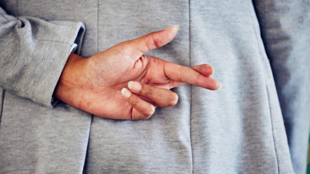 A person crosses their fingers behind their back, representing a lying in an interview